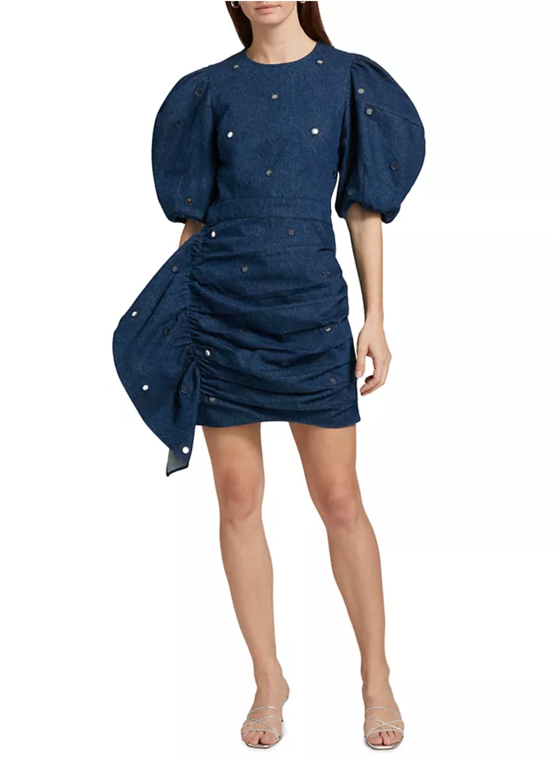 A person in a navy Pia Mini Dress by Rhode, featuring puffed short sleeves, a ruched asymmetric skirt with delicate embellishments, elegantly draped on one side, paired with transparent heels.