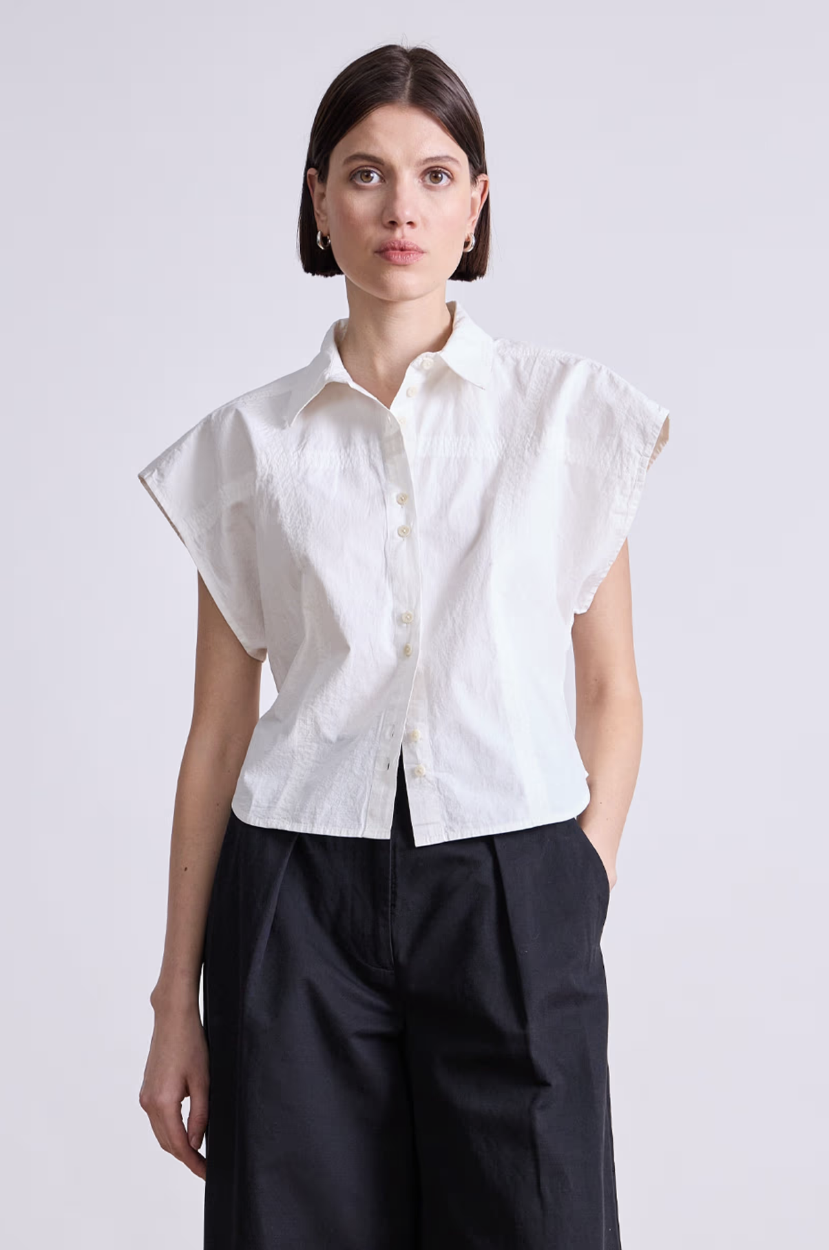 A person with short brown hair wears the Apiece Apart Toni Sleeveless Top in white and black wide-leg pants, standing against a plain light background.