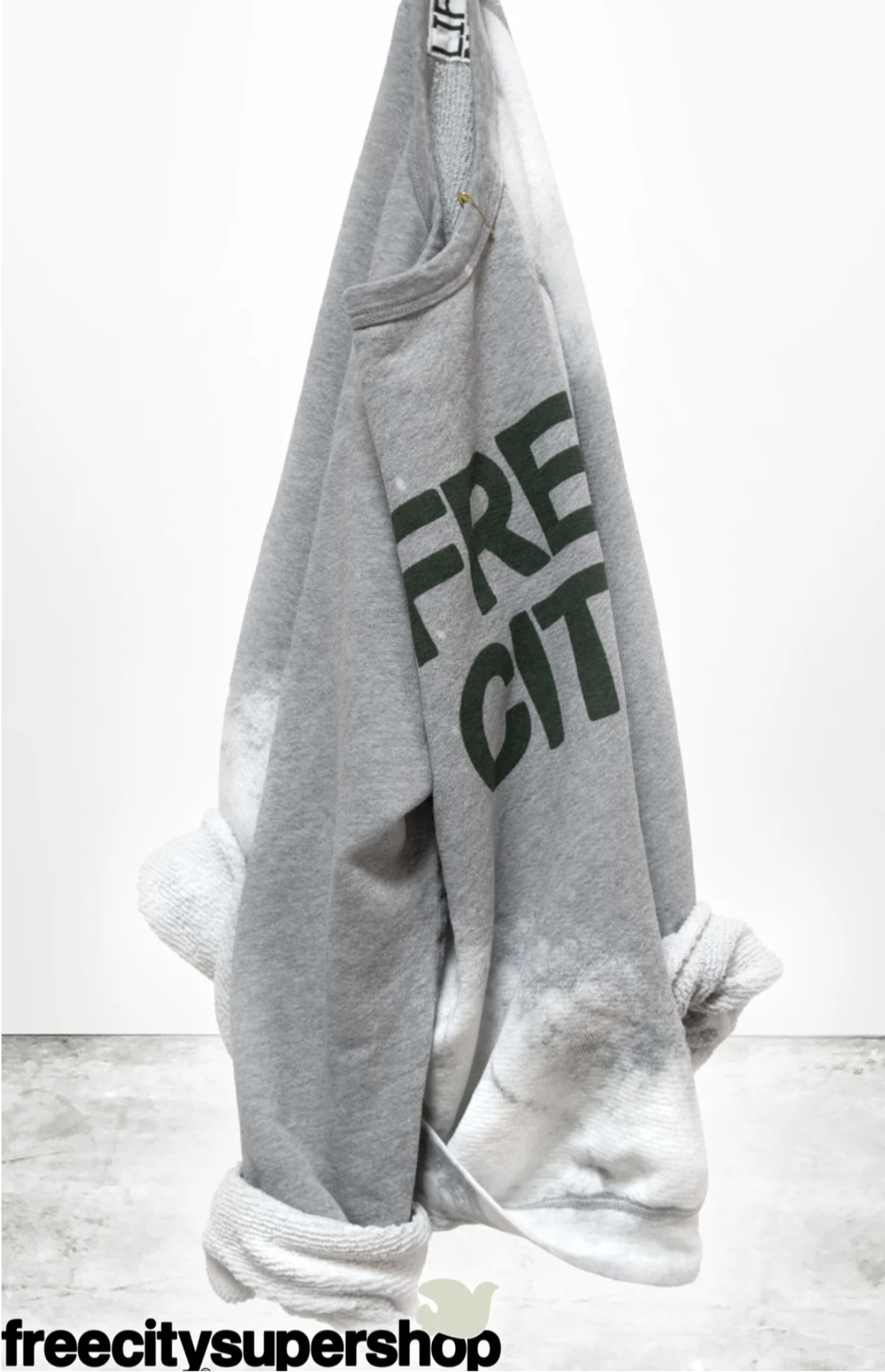The FREECITY BLEACHOUT RAGLAN by Free City (sparrow, LLC) is a gray raglan sweatshirt with green "FREE CITY" lettering and lighter tie-dye effect cuffs. Made in the USA and hand-screen printed. "freecitysupershop" is shown at the bottom.