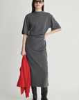 Luna Cinched Maxi dress by Apiece Apart styled with black boots and sunglasses, red coat in hand, neutral backdrop.