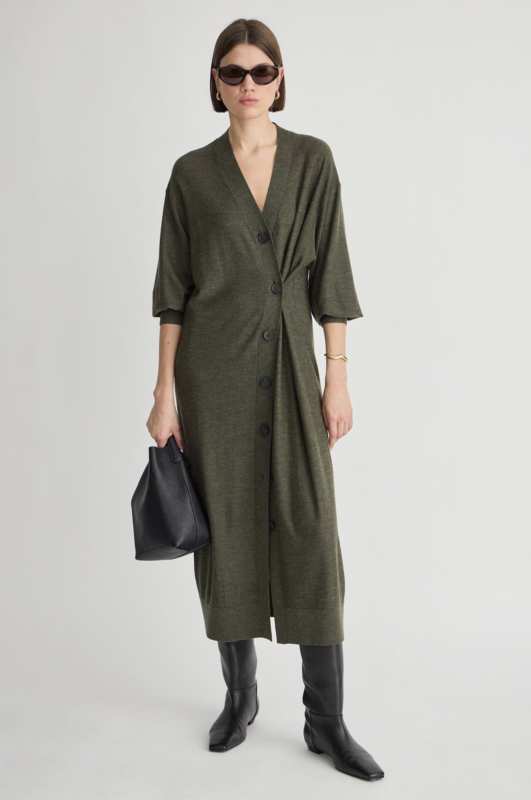 Olive green Drippy Cardi Dress by Apiece Apart styled with black boots and accessories on a white backdrop.
