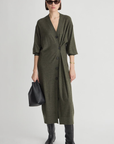 Olive green Drippy Cardi Dress by Apiece Apart styled with black boots and accessories on a white backdrop.
