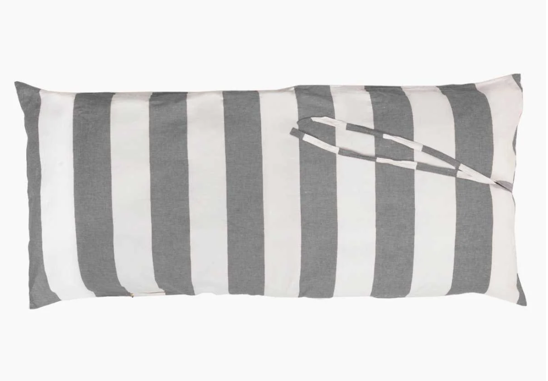 A Hedgehouse THROWBED COVER IN CHARCOAL STRIPE with wide, vertical stripes in alternating shades of gray and white. Another piece of fabric with matching stripes is draped over the pillow, creating a loop. The machine washable cover makes it versatile for both indoor and outdoor use. The pillow is set against a plain white background.