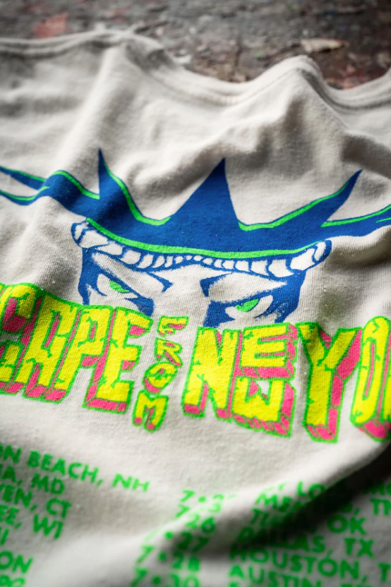 A close-up of a RAMONES ESCAPE FROM NEW YORK VINTAGE WHITE by Made Worn with bright, colorful graphics. The design features a stylized blue and green face with spiky hair above the text "NYC" in neon yellow and pink. Below the text, some dates and locations including Scottsdale Arizona are listed in green. The fabric is slightly wrinkled.