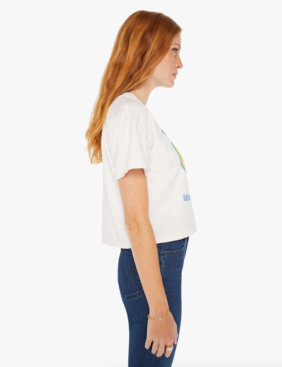 A person with long red hair stands in a side profile view against a white background, reminiscent of the vibrant sunset hues in Scottsdale, Arizona. They are wearing THE GRAB BAG CROP TEE DONT WORRY with short sleeves and blue jeans. Their left arm hangs naturally by their side, and their gaze is directed forward.