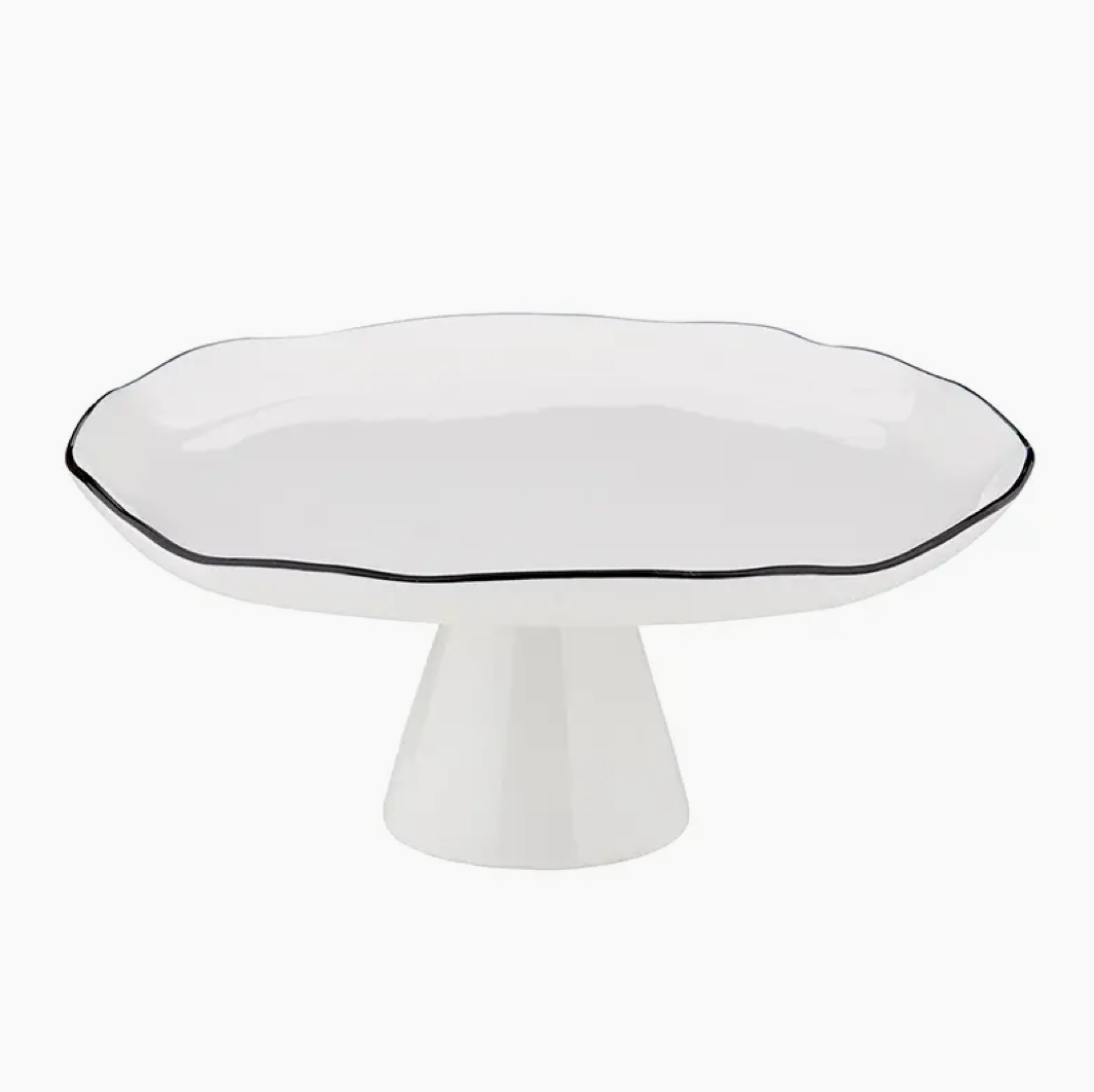 White ceramic **Pedestal Tray - Black** by **Faire** on a pedestal base with a slightly wavy edge and thin black rim, perfect for adding a touch of Scottsdale Arizona elegance to your bungalow kitchen.