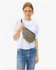 A woman with red hair wearing a white blouse and Arizona-style blue jeans holds a Clare Vivier Grande Fanny Woven Checker shoulder bag. She stands against a plain background.