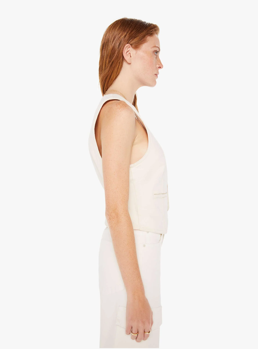 Side profile of a woman in a white sleeveless top and matching pants, standing against a plain white background. She has her hair neatly styled in an Arizona-inspired look and is looking to the side while wearing The Masked Rider by Mother.