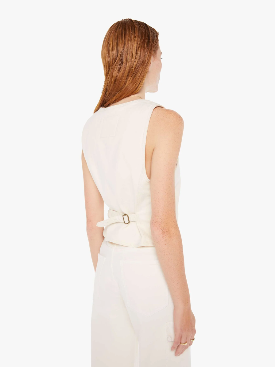 A woman with shoulder-length red hair is standing with her back to the camera, wearing a chic white sleeveless top and white pants, featuring a belt detail at the back, showcasing Mother style.