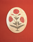 Round decorative Mughal Oval Tray with a floral design featuring red poppies and green leaves on a cream background, displayed against a vibrant red backdrop in a Scottsdale Arizona bungalow.