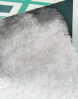 A mound of Flaky Maldon Sea Salt spilling out from a partially opened Faire green and white cardboard box on a white background.