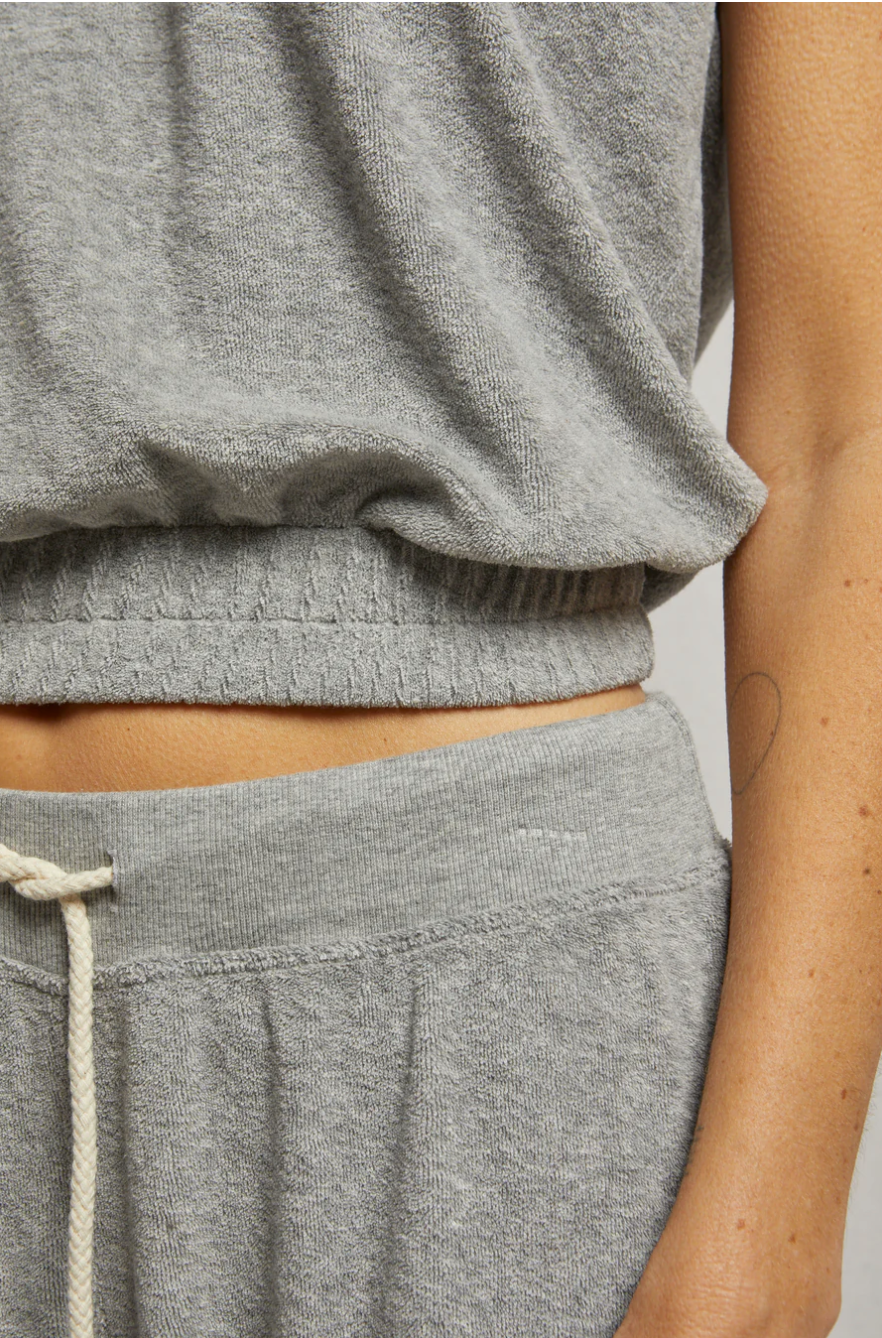 A close-up of a person wearing the Perfectwhitetee ELLIE terry banded tank—loose-fitting, light grey with a scoop neckline—paired with matching drawstring pants. The person&#39;s midriff and a simple line tattoo on their arm are visible.