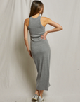 A person with long hair is standing with their back to the camera, wearing a sleeveless, gray, body-hugging Cassidy Blondie Dress by Perfectwhitetee and silver sneakers. Their left hand is resting on their hip, and they are set against a plain, light-colored fabric background.