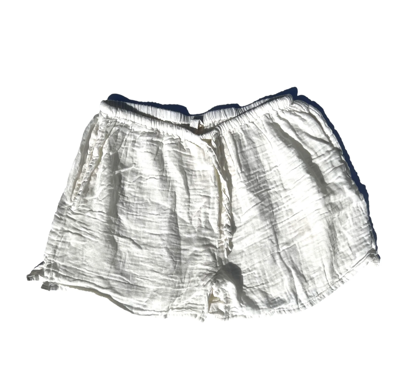 A pair of white, cotton Hawaiian Beach Shorts from By the Sea Organics with an elastic waistband and a drawstring waist. The shorts have a wrinkled texture and are laid flat against a plain white background.