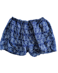 A pair of Hawaiian Beach Shorts in blue by By the Sea Organics, complete with an elastic drawstring waist. They feature a pattern of white, irregular vertical lines resembling streaks or dashes. The 100% organic fabric appears lightweight and slightly crinkled.