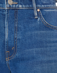 Close-up image of a pair of blue denim jeans. The image shows the top part of The Swisher Sneak Fray by Mother with visible stitching, a button closure, belt loops, and part of the front pocket. The fabric features a classic blue wash with slight color variations.