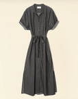 A long Linnet Dress by Xirena, crafted from dark grey denim, featuring short sleeves, a button-down front, a fabric belt at the waist, and side slits at the hem. The tailored fit dress is hanging against a plain beige background.