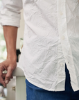 A person wearing a wrinkled BARRY CRINKLE Shirt and blue jeans stands next to a counter. The shirt label reads "Frank & Eileen, est. 1947" and boasts being made of 100% cotton. The background is blurred, focusing attention on the clothing.