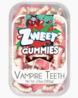 A rectangular container labeled "Halloween Gummies" from the brand Faire holds pink and white gummy candies shaped like vampire teeth. The label features a cartoon vampire with fangs and a cape, emphasizing their fruity flavor. The container states "Vampire Teeth, Net Wt. 10oz (285g)" and comes in a shareable batch for all to enjoy.