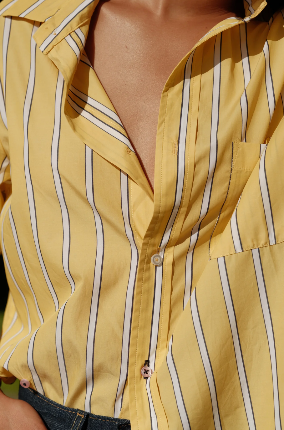 Close-up of a person wearing Cissa's The MEN'S Shirt, a yellow garment with blue and white vertical stripes. Made from soft Egyptian cotton, this shirt features a single chest pocket and is partially unbuttoned at the top, with the lower buttons fastened, revealing a small portion of the person's chest.