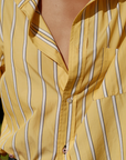 Close-up of a person wearing Cissa's The MEN'S Shirt, a yellow garment with blue and white vertical stripes. Made from soft Egyptian cotton, this shirt features a single chest pocket and is partially unbuttoned at the top, with the lower buttons fastened, revealing a small portion of the person's chest.