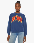 A person stands wearing The Biggie Concert raglan sweatshirt by Mother, crafted from super-soft cotton and showcasing a vibrant, 80s-inspired graphic in the center. Their hair is styled in a high bun, and they pair the sweatshirt with light blue jeans and delicate jewelry. The plain white background highlights the full focus on them and their outfit.