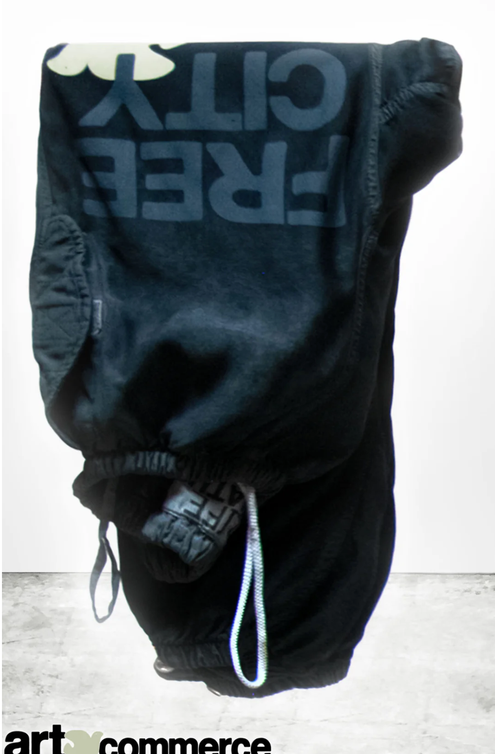 An upside-down view of the Flap/Snap LG MATTE/SATIN AirJump Pant with the text &quot;FREE CITY&quot; printed in large letters on the leg. The pants, in a custom sunfade wash, are showcased against a simple, light-colored background. The brand logo &quot;art commerce&quot; is partially visible at the bottom.