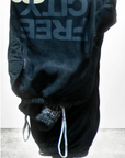 An upside-down view of the Flap/Snap LG MATTE/SATIN AirJump Pant with the text "FREE CITY" printed in large letters on the leg. The pants, in a custom sunfade wash, are showcased against a simple, light-colored background. The brand logo "art commerce" is partially visible at the bottom.