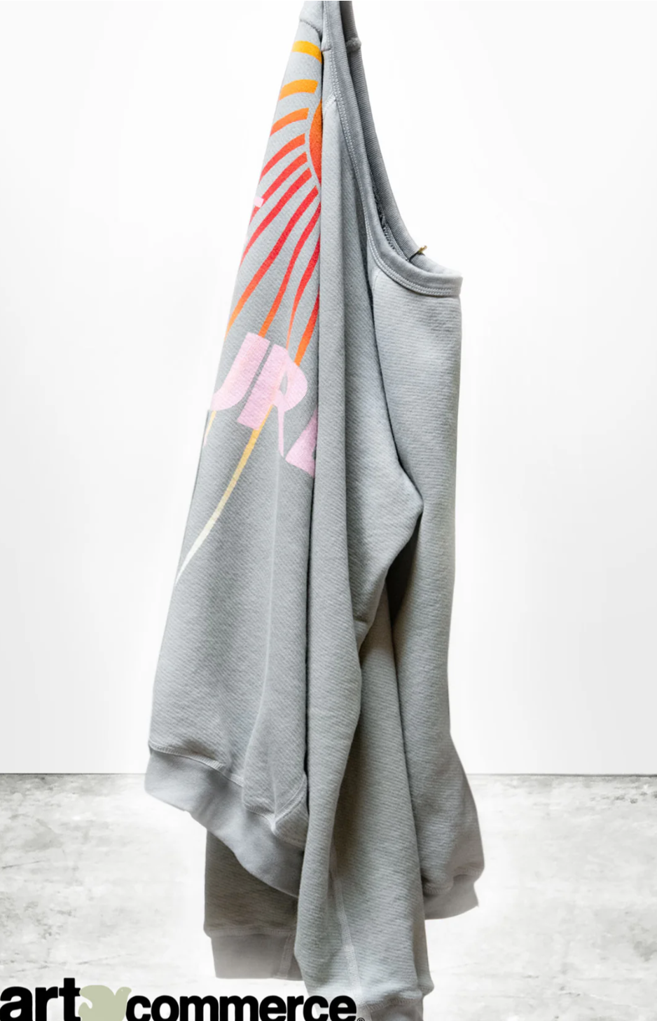 An LNLSUN SprYum Biggie Raglan sweatshirt from Free City (sparrow, LLC) hangs on a hanger against a plain white background. The back features pastel-colored graphic designs in shades of pink, orange, and yellow thanks to a custom supersaturated sunfade dye process. The brand logo &quot;art commerce&quot; is visible at the bottom.