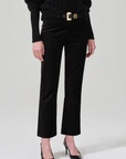 A person stands against a plain background wearing the Isola Cropped Trouser in Velvet by Citizens Of Humanity/AGOLDE, paired with a black pullover and black heeled shoes. They accessorize with a wide belt featuring a large gold buckle and wear a simple gold ring on their left hand.