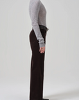 A person stands in profile against a plain background, wearing a long-sleeve grey sweater tucked into high-waist Annina 30 Zip Fly In Corduroy pants by Citizens Of Humanity/AGOLDE. They have on black pointed-toe heels and a black belt. Only the lower part of their face is visible.