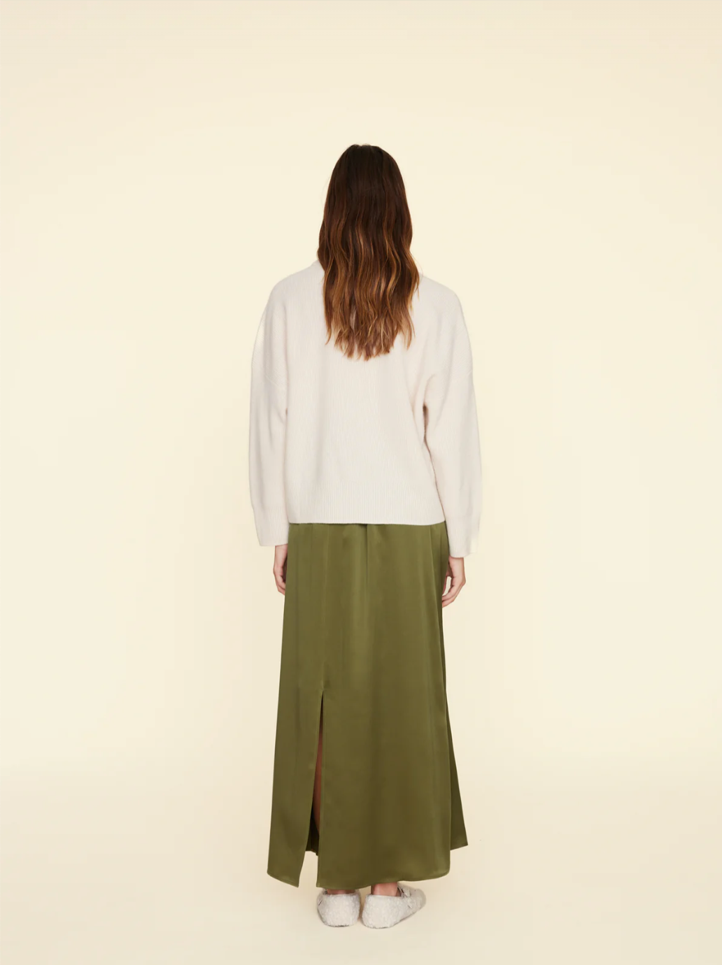 The Sela Skirt by Xirena, a midi-length, olive-green piece with a straight cut, is shown against a plain beige background. Made of luxurious silk charmeuse and featuring an elastic waistband, this slip-on skirt exudes effortless elegance.