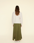 The Sela Skirt by Xirena, a midi-length, olive-green piece with a straight cut, is shown against a plain beige background. Made of luxurious silk charmeuse and featuring an elastic waistband, this slip-on skirt exudes effortless elegance.