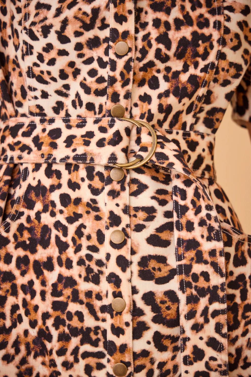 Take a closer look at the Robinson Dress by Hunter Bell NYC, an essential addition to your wardrobe with its striking leopard print fabric. This eye-catching piece is designed with a belt adorned with a round metal buckle and cascading buttons down the front, showcasing a vibrant mix of brown, black, and beige hues reminiscent of wild leopard spots.