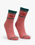 Two pink "Baby Steps" tube socks by Mother, featuring dark green accents and a red logo near the top, styled like a Rodeo Queen's. The socks are displayed standing upright on a white background.