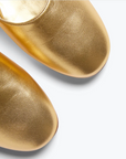 Close-up of two gold Freda Salvador AUBREY Flats on a white background, highlighting their shiny texture, rounded toes, and a comfortable padded leather footbed.