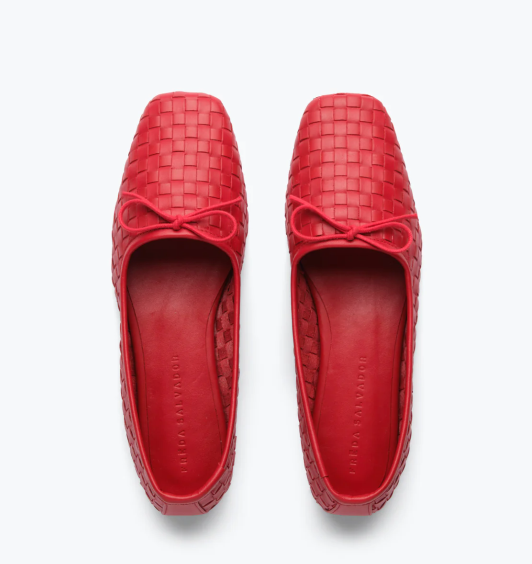 The JADA Flat by Freda Salvador is a pair of red woven ballet flats made from Spanish leather, featuring square toes and small bows on top, displayed from an overhead view against a white background.