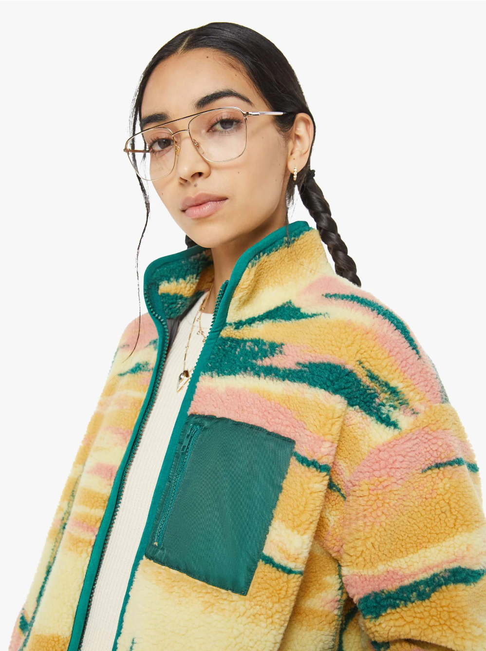 A person with long dark hair in braids is wearing glasses and The Heat Lamp Cactus Cooler, a colorful, patterned fleece jacket from Mother, featuring balloon sleeves. The jacket boasts a high collar and a teal chest pocket, artfully capturing the vibrant hues of a desert sunset graphic against the white background.