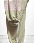 The SUPERFLUFF Lux OG Sweatpants from Free City (Sparrow, LLC) showcase pink and white hand-screen printed "FREE CITY" text on the side against a plain background. These olive green unisex sweatpants are made from lightweight French terry and feature an elastic waistband with a drawstring, as well as gathered cuffs for added comfort.