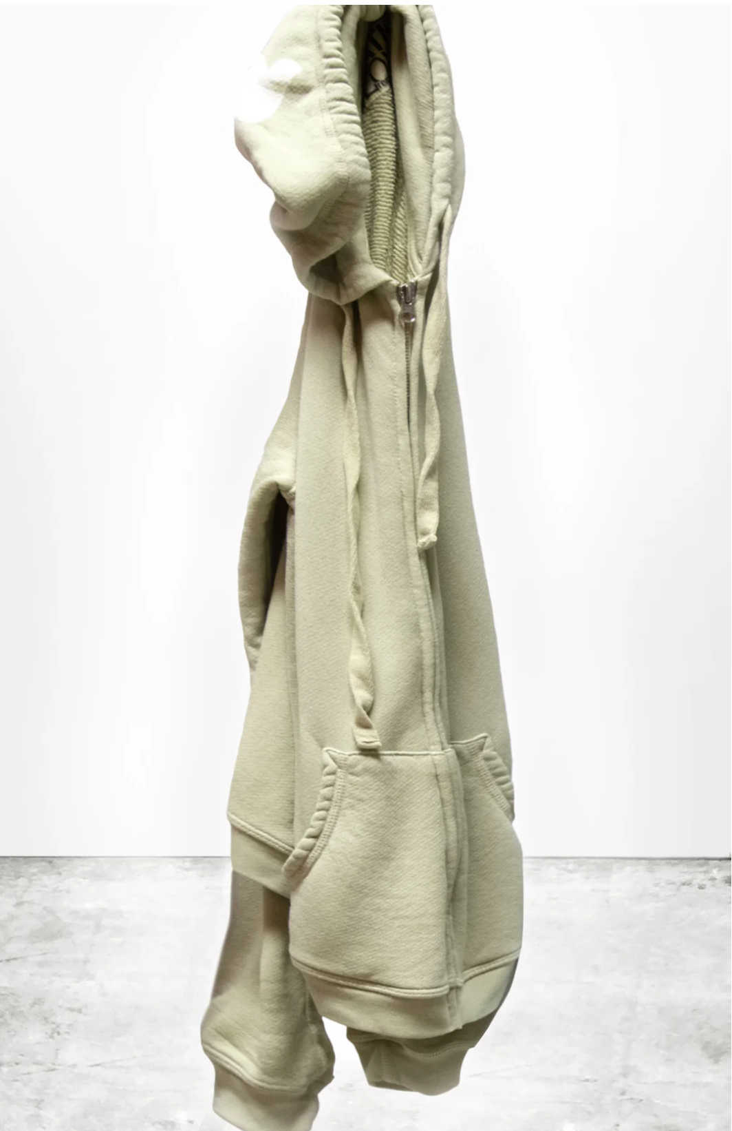 A beige Free City SUPERFLUFF Lux Zip Hoodie from Sparrow, LLC is displayed against a plain white background. The hood, sleeves, and front pockets are visible, highlighting the lightweight French terry fabric that looks soft and warm.