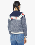 Rear view of a person with braided hair, wearing "The Try Outs" cardigan sweater by Mother in marled navy cotton and alpaca, featuring floral patterns on the shoulders. They also have on blue jeans. The background is plain white.