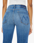 A person is shown from the rear wearing The Tripper Ankle Fray high-rise flare jeans by Mother, crafted in Los Angeles. These jeans feature back pockets with an embroidered design and are paired with a white top and a small ring on the person's left hand.