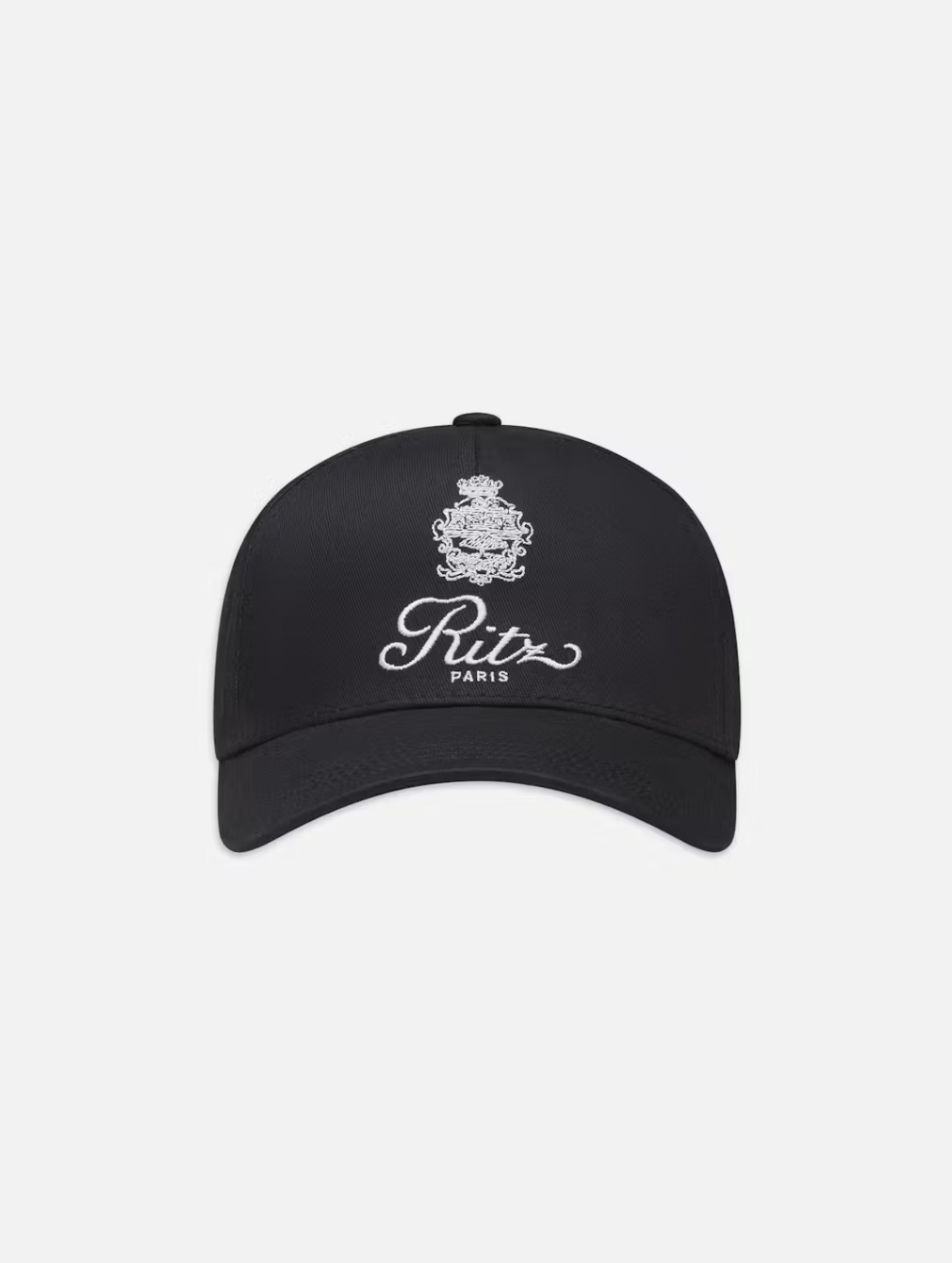 The FRAME Ritz Cotton Trucker is a classic black baseball cap crafted from 100% cotton, featuring the iconic Ritz Paris logo with an emblem above "Ritz Paris" in elegant white script on a clean white background.