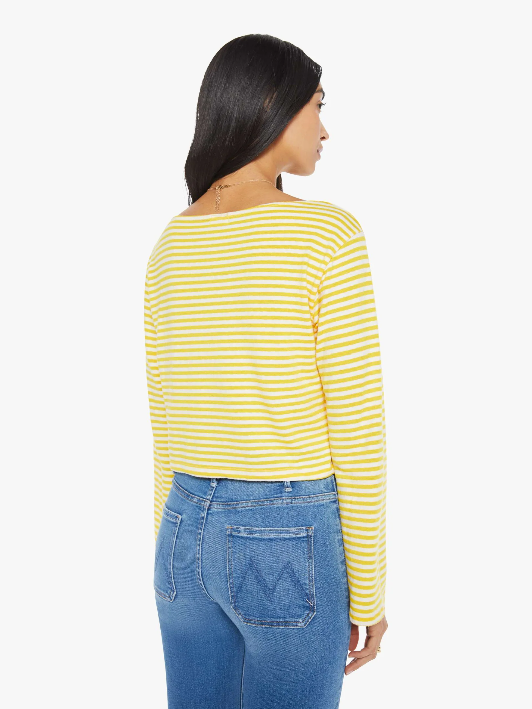 A person with long dark hair is wearing Mother's The Skipper Bell LS Tee, featuring yellow and white horizontal stripes, along with blue jeans. They stand facing away from the camera against a plain white background.