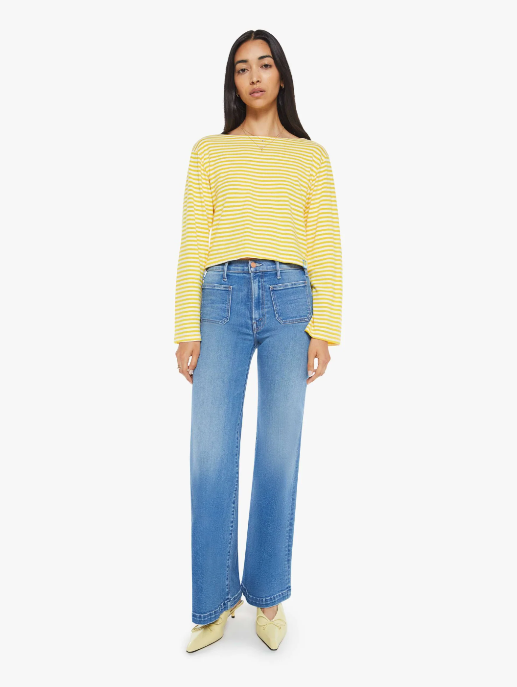 A person confidently models The Skipper Bell LS Tee by Mother, featuring yellow and white horizontal stripes, paired with blue wide-leg jeans against a plain white background. Their light-colored pointed shoes accentuate the effortless style of this boat neck top.