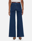 A person is seen from behind wearing FRAME's Le Slim Palazzo Modernist jeans, a high-rise wide-leg design in dark blue super stretch denim with large back pockets. They're paired with heeled shoes and a white top against a plain white background.