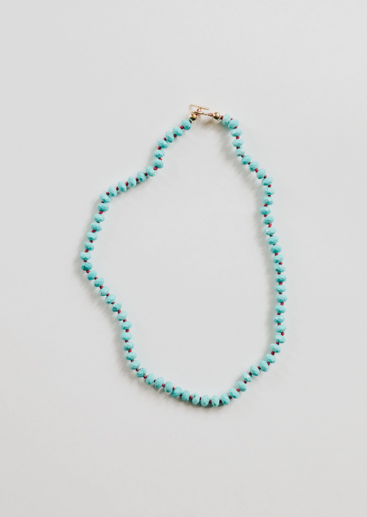 The Faire Gemstone Necklace features turquoise and brown beads crafted from natural gemstones in a loop on a light background. Slightly irregular for texture, it includes an elegant small gold-filled clasp.