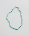 The Faire Gemstone Necklace features turquoise and brown beads crafted from natural gemstones in a loop on a light background. Slightly irregular for texture, it includes an elegant small gold-filled clasp.