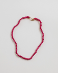 The Faire Gemstone Necklace showcases elegance with its small round pink beads and a gold-filled clasp, arranged in an oval shape on a white background, highlighting the beauty of handmade jewelry.