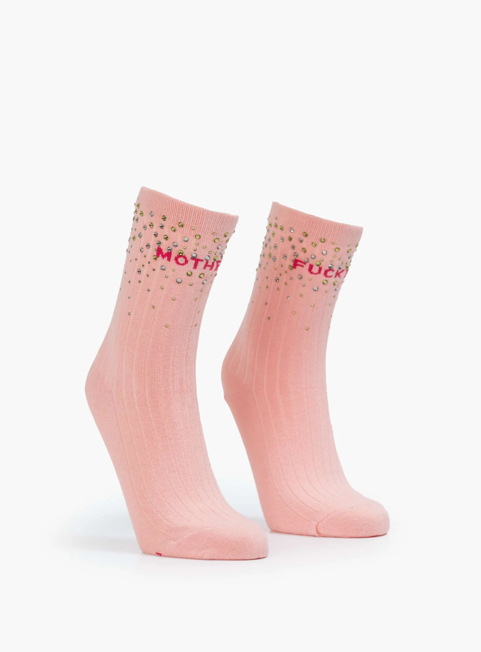 Two baby pink tube socks from Mother, named "The Half Step," stand upright against a white background, featuring a ribbed texture. They are adorned with colorful crystal embellishments at the top and have bold red text across them.